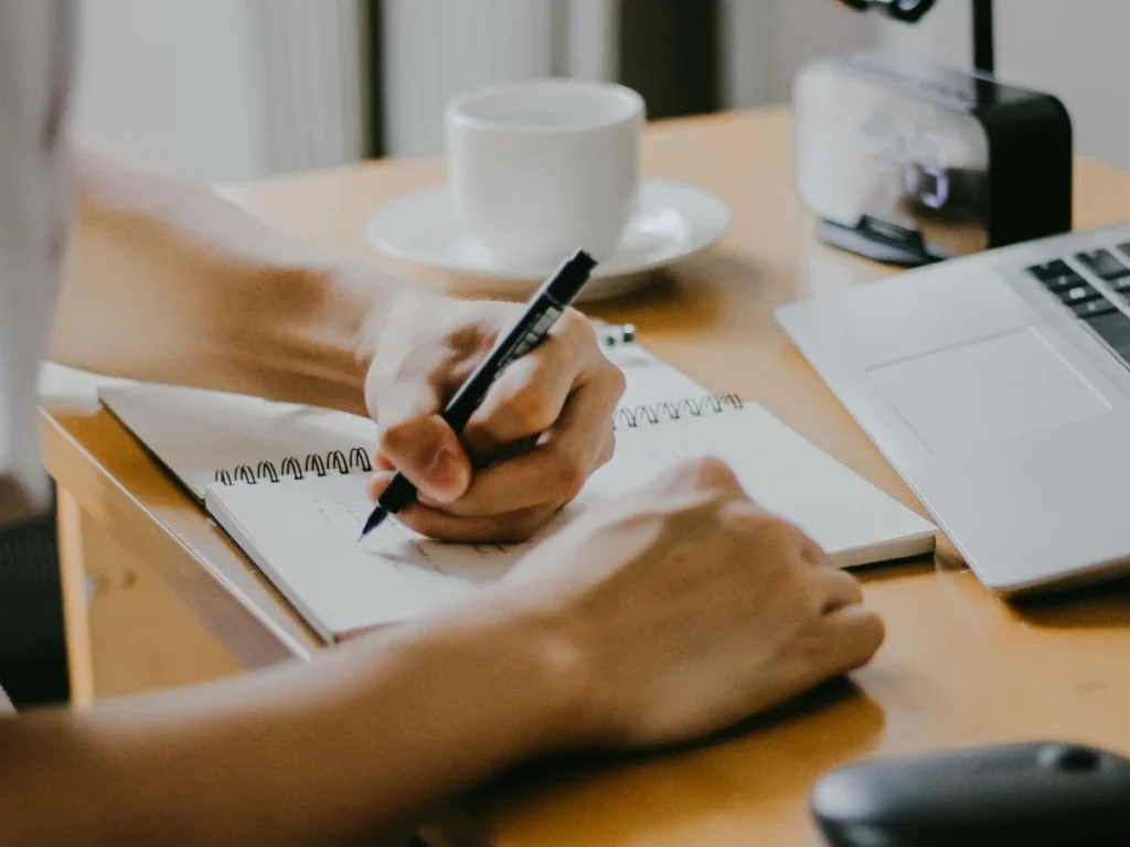 A close up of a DUI online class student writing down notes with his laptop in front of him.