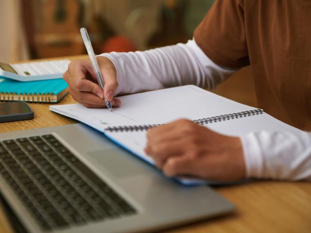 A close-up shot of a student writing notes with her laptop in front of her.