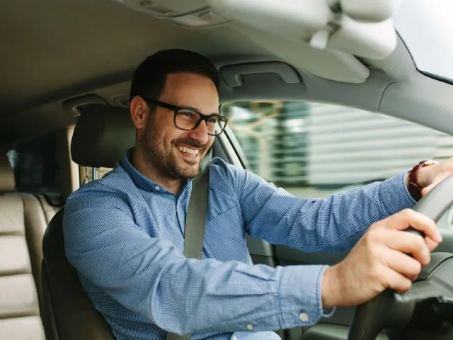 A man with glasses smiling while driving his car.