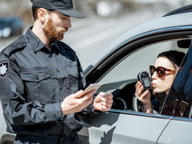 A police officer checks a female driver’s BAC level with a breathalyzer.