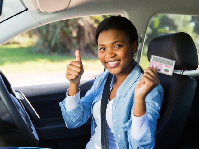 A woman smiles while holding out a thumbs up and her reinstated driver’s license.