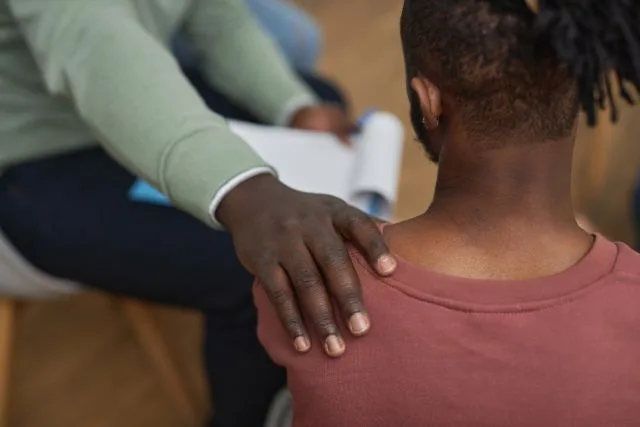A man’s hand placed on another man’s shoulder, consoling and supporting him