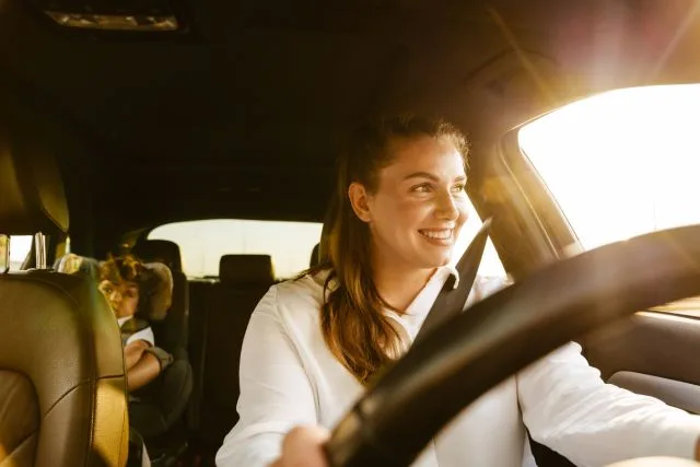 A smiling mom driving the car with her child at the backseat