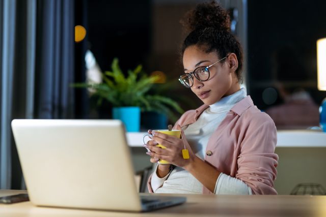 A young woman is attending her online DUI class on a laptop while drinking tea