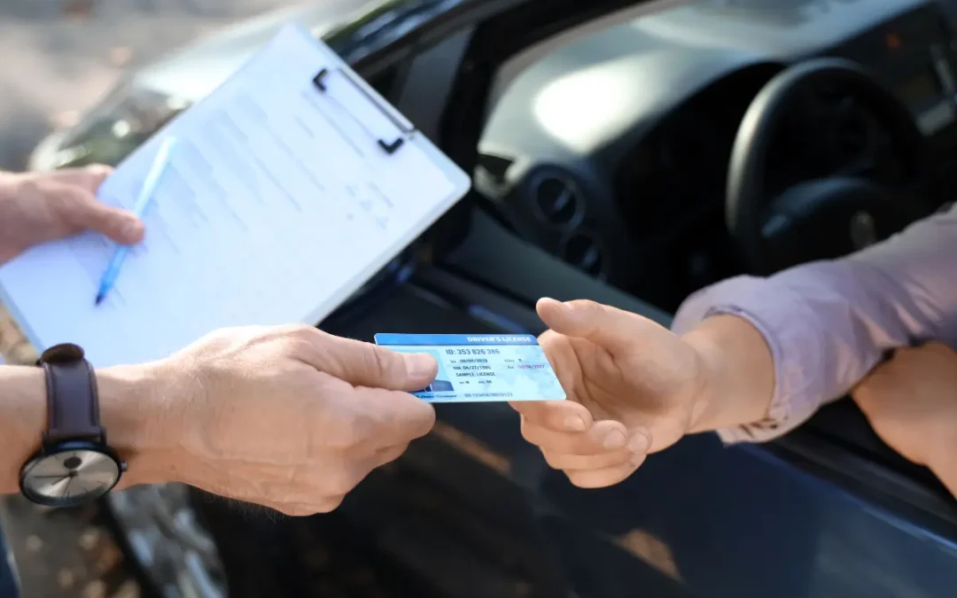 A man hands over a reinstated driver's license to a person inside a car.