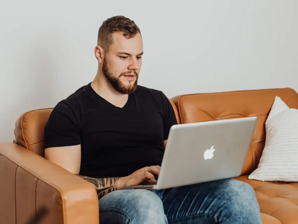 A man sits in a couch at home while taking online DUI classes on his laptop.